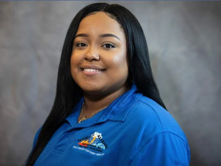 Smiling woman with long black hair wearing a blue polo shirt against a gray background.